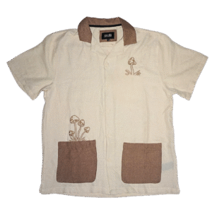 👕 Camisa de manga corta color marfil con textura estilo lino marca Malibu by Drill Clothing Co. Cuello y dos bolsillos de parche en color marrón. Bordados de hongos marrones en pecho y bolsillo
