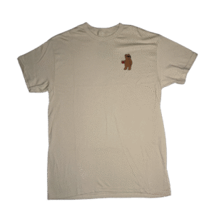 🐻 Remera color tan beige de corte estándar para hombre o mujer marca Riot Society. Pequeño logo bordado en el pecho de un oso de peluche marrón con gafas de sol sosteniendo un vaso con una bebida roja
